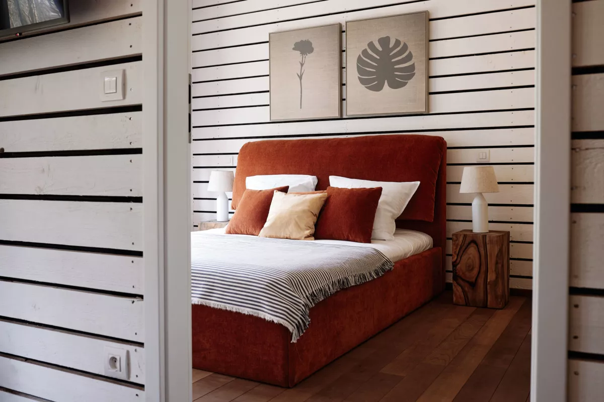 La chambre du rez-de-chaussée : lit double 160 × 200 à tête de lit rouille, lampes de chevet et murs en lambris blanc