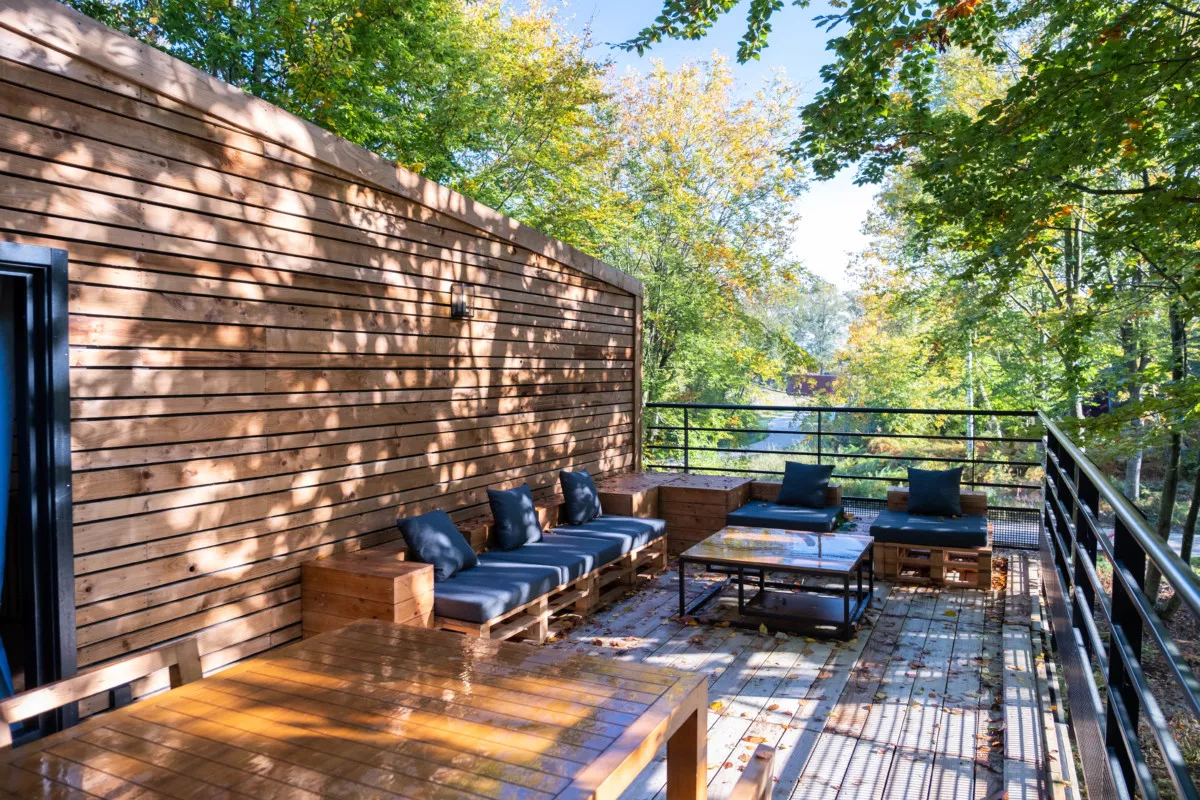 La terrasse perchée dans les arbres, avec salon d'extérieur et table en bois, baignée de soleil
